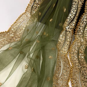 May include: Olive green sheer fabric with gold sequin and bead embellishments. The fabric has a delicate, flowing drape, with intricate gold floral patterns along the edges. The design features a combination of sequins and small beads.