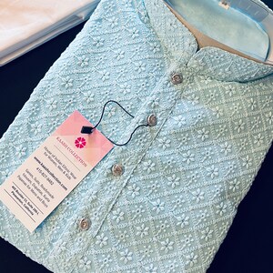 Pu&ograve; includere: Una kurta ricamata di colore azzurro chiaro con colletto alla coreana e chiusura con bottone. La kurta presenta un delicato motivo floreale ed &egrave; realizzata in un tessuto leggero. L'etichetta sulla kurta riporta "Kaash Collection" e include informazioni di contatto e un indirizzo del sito web.