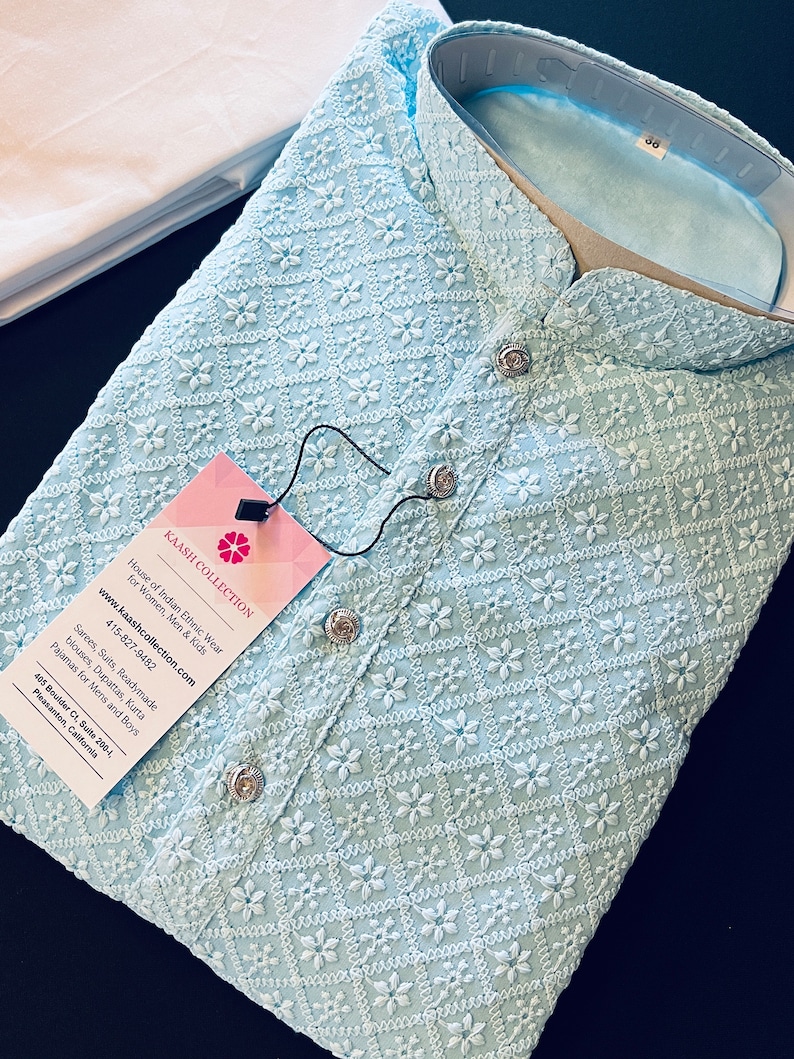 Pu&ograve; includere: Una kurta ricamata di colore azzurro chiaro con colletto alla coreana e chiusura con bottone. La kurta presenta un delicato motivo floreale ed &egrave; realizzata in un tessuto leggero. L'etichetta sulla kurta riporta "Kaash Collection" e include informazioni di contatto e un indirizzo del sito web.