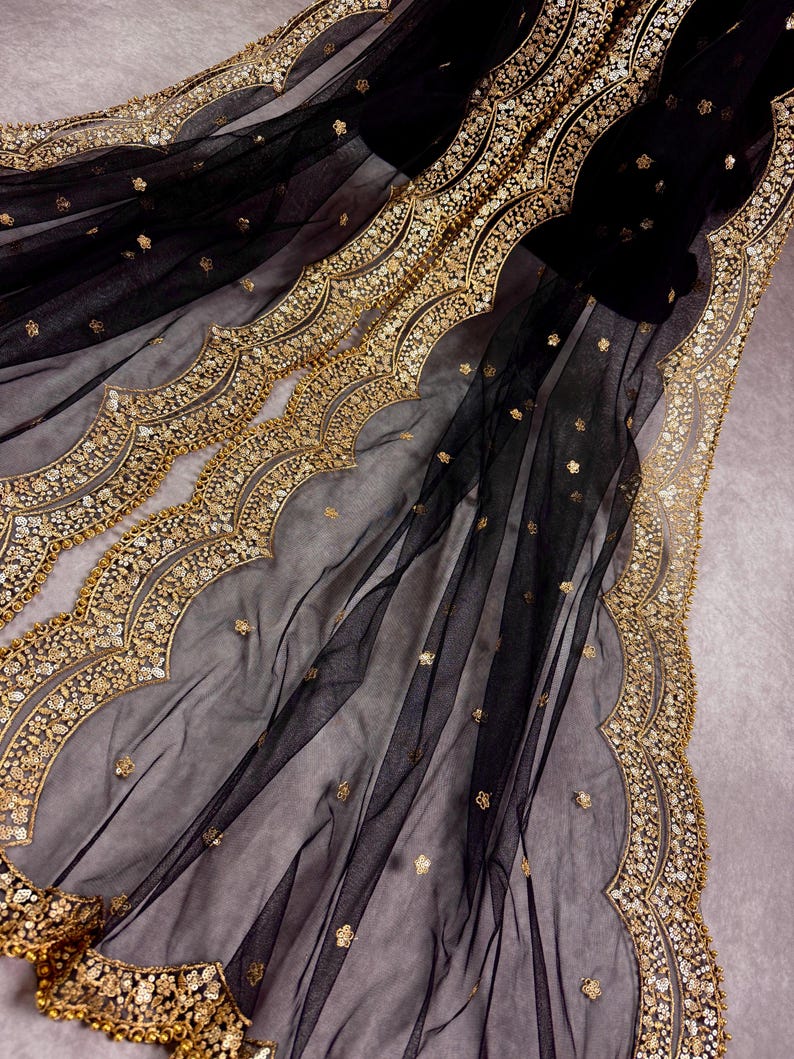 May include: Black sheer fabric with gold embroidery and scalloped edges. The fabric is delicate and has a luxurious feel.