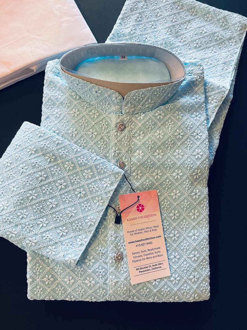 Pu&ograve; includere: Una kurta ricamata di colore azzurro chiaro con un motivo floreale bianco. La kurta ha un colletto alla coreana e una chiusura con bottone. L'etichetta sulla kurta recita "KAASH COLLECTION House of Indian Ethnic Wear for Women, Men & Kids www.kaashcollection.com 415-827-0482 Sarees, Suits, Readymade blouses, Dupattas, Kurta Pajamas for Mens and Boys 428 Boulder Ct, Suite 206-L Pleasanton, California"