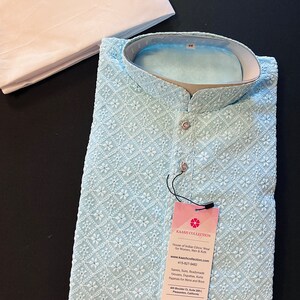 Pu&ograve; includere: Una kurta ricamata di colore azzurro chiaro con colletto bianco e chiusura con bottone. La kurta &egrave; realizzata in un tessuto morbido e leggero, perfetta per il clima caldo. L'etichetta sulla kurta riporta "Kaash Collection" e include il sito web e il numero di telefono dell'azienda.