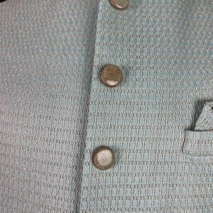 May include: A light blue jacket with a fine, woven pattern and four brown buttons.