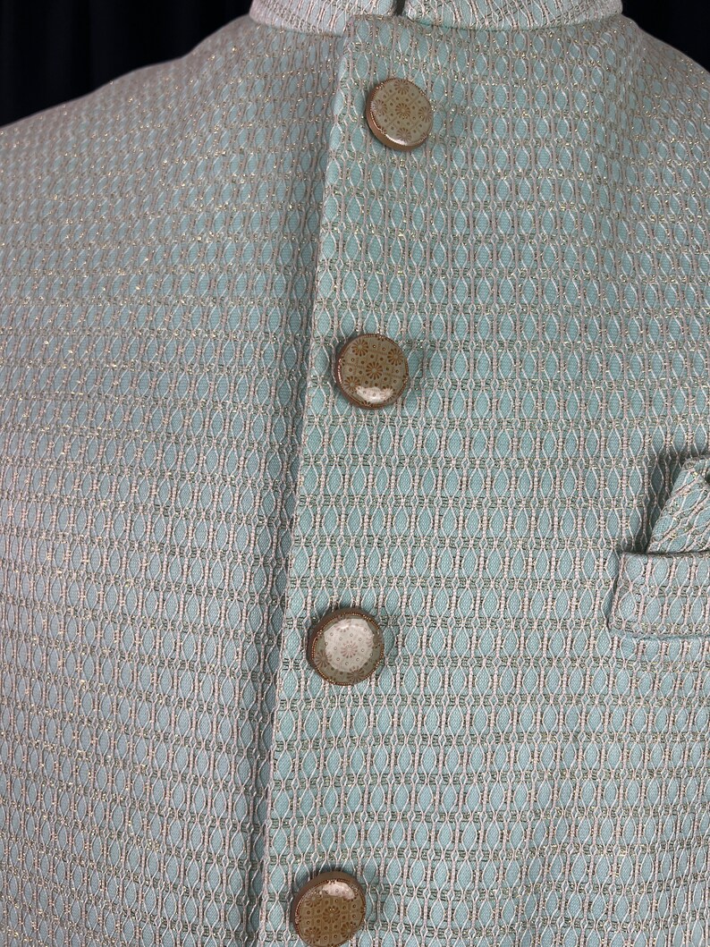 May include: A light blue jacket with a fine, woven pattern and four brown buttons.