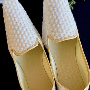 Pode incluir: Um par de chinelos brancos bordados com detalhes dourados. Os chinelos t&ecirc;m um tecido texturizado e uma palmilha macia e acolchoada.