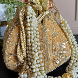 May include: A gold and ivory embroidered drawstring bag with a pearl and gold tassel. The bag is decorated with sequins and beads.