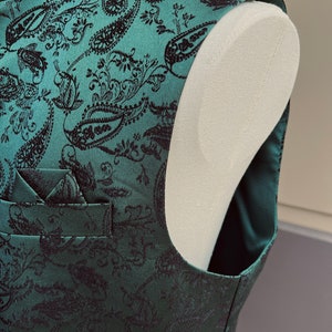 May include: A green paisley patterned vest with a black pocket square. The vest is made of a soft, luxurious fabric and has a classic, timeless design.