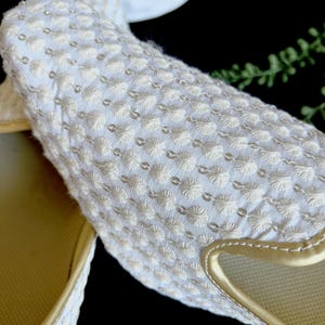 Pode incluir: Um par de chinelos brancos bordados com acabamento dourado. Os chinelos t&ecirc;m um design acolchoado texturizado.