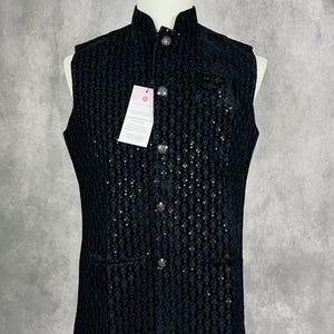 May include: A black sequined vest with a mandarin collar and button closure. The vest has two pockets on the front and is sleeveless.