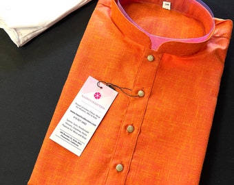 May include: Orange cotton kurta with a mandarin collar and button closure. The kurta has a textured fabric and is accompanied by a white cotton dupatta.