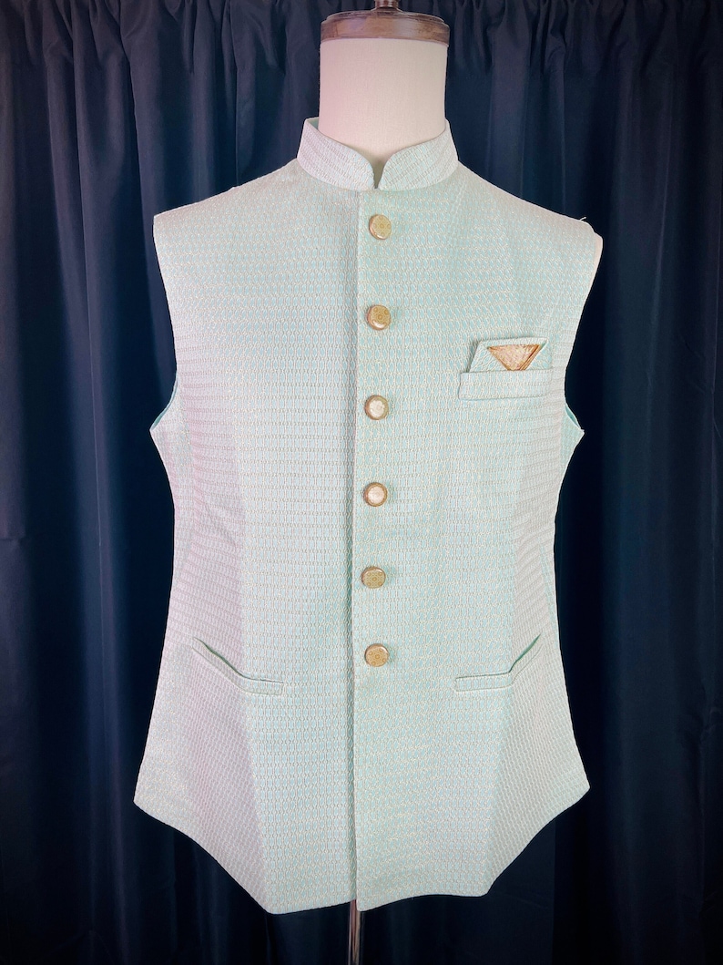 May include: A light green sleeveless vest with a mandarin collar and gold buttons. The vest has a pocket on the right side with a gold embroidered design.