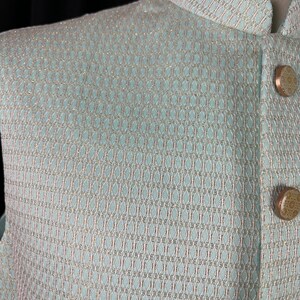 May include: A light blue vest with a subtle geometric pattern woven into the fabric. The vest has a mandarin collar and gold buttons.