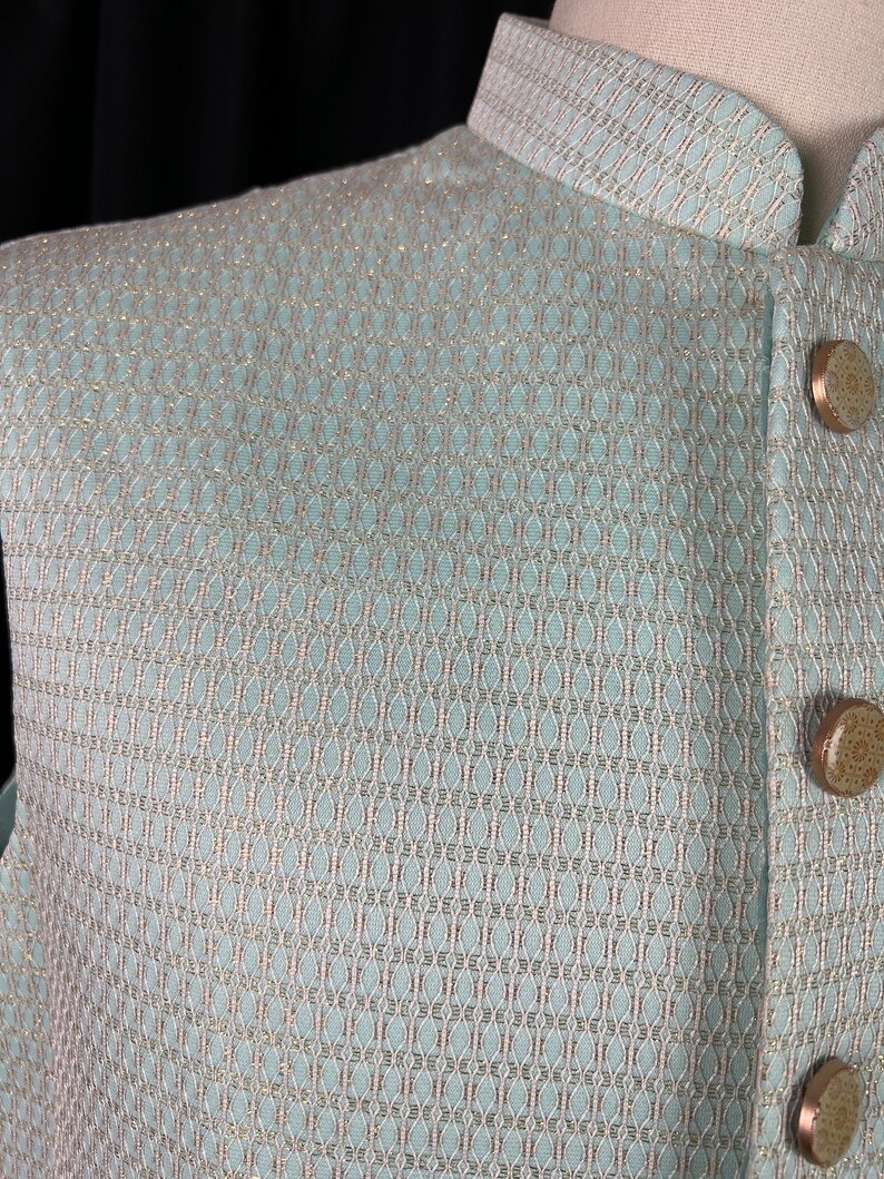 May include: A light blue vest with a subtle geometric pattern woven into the fabric. The vest has a mandarin collar and gold buttons.