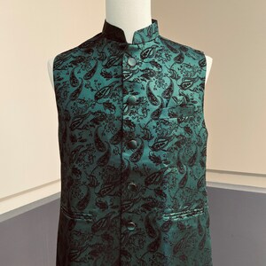May include: A dark green sleeveless vest with a paisley pattern and black buttons. The vest has a mandarin collar and a pocket on the left side.