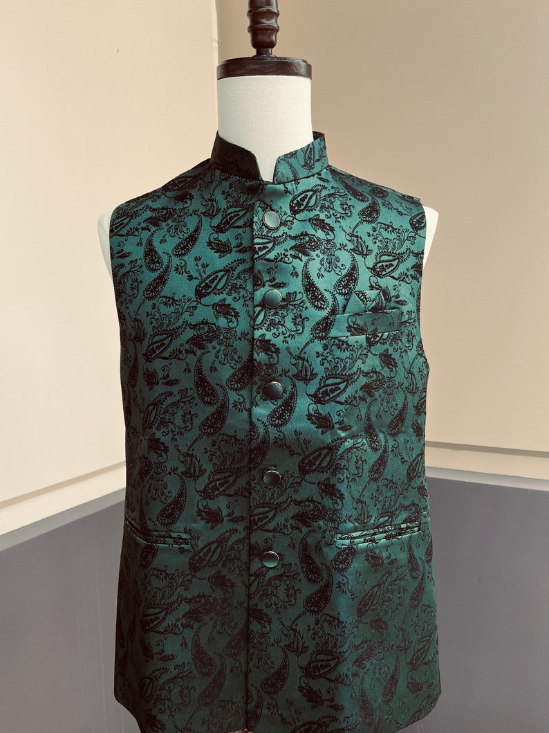 May include: A dark green sleeveless vest with a paisley pattern and black buttons. The vest has a mandarin collar and a pocket on the left side.