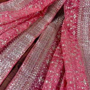 Peut inclure: Gros plan sur un tissu fluide et transparent de couleur rose vif. Le tissu est orn&eacute; de broderies et de sequins argent&eacute;s complexes, cr&eacute;ant un effet scintillant. Le motif pr&eacute;sente des motifs floraux et g&eacute;om&eacute;triques.