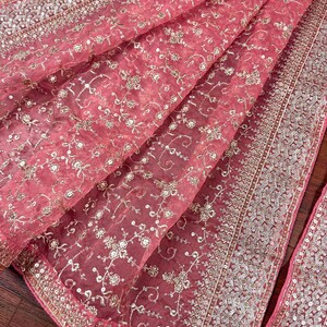 Peut inclure: Un tissu rose transparent drap&eacute; avec une broderie argent&eacute;e complexe. Le tissu pr&eacute;sente un motif floral et est bord&eacute; d'une garniture &agrave; paillettes d&eacute;taill&eacute;e. Le mat&eacute;riau d&eacute;licat est pli&eacute;, mettant en valeur sa texture et son design.