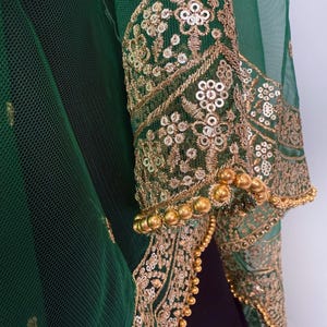 Peut inclure: Gros plan sur un v&ecirc;tement vert avec des broderies et des sequins dor&eacute;s. Les manches sont orn&eacute;es de motifs floraux et d'une bordure perl&eacute;e. Le tissu est une maille transparente, superpos&eacute;e &agrave; un tissu plus fonc&eacute;.