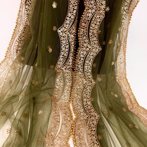 May include: Olive green sheer fabric with intricate gold sequin and bead embellishments. The design features ornate, flowing patterns along the edges and center, creating a luxurious and elegant aesthetic. The fabric is draped, showcasing its delicate texture.
