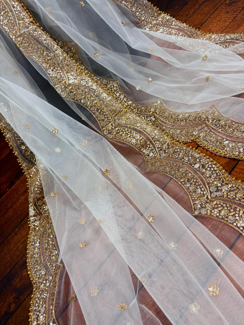 May include: White sheer fabric with a gold embroidered border. The border features a repeating pattern of floral and geometric designs.