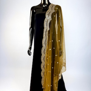 May include: A black dress is draped with a sheer, golden-yellow dupatta. The dupatta features intricate gold embroidery along the edges and scattered embellishments. The mannequin is black and stands against a white backdrop.