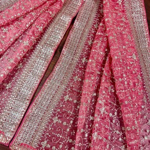 Peut inclure: Gros plan sur un tissu rose avec des broderies argent&eacute;es et dor&eacute;es complexes. Le tissu est pli&eacute;, r&eacute;v&eacute;lant plusieurs couches et textures. La broderie pr&eacute;sente des motifs floraux et g&eacute;om&eacute;triques, cr&eacute;ant un design luxueux et d&eacute;taill&eacute;.