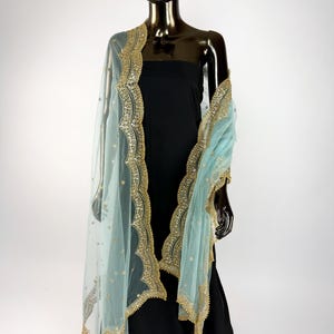 May include: A pale blue sheer dupatta with gold embroidery and embellishments. The dupatta is draped over a black dress on a mannequin. The gold trim has a scalloped edge. The dupatta has small gold dots throughout.