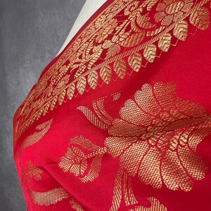 May include: A red textile with a gold floral pattern. The fabric is draped, showcasing the intricate design of flowers and leaves. The border features a detailed gold leaf pattern, adding a touch of elegance to the overall design.
