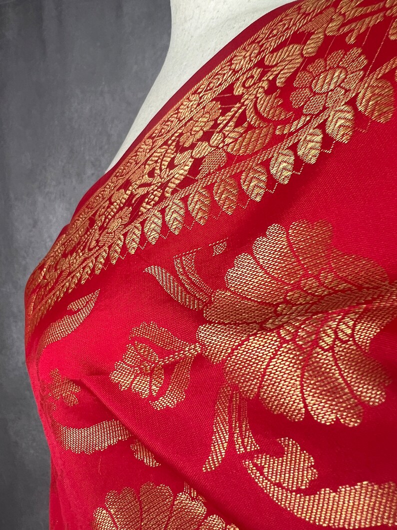 May include: A red textile with a gold floral pattern. The fabric is draped, showcasing the intricate design of flowers and leaves. The border features a detailed gold leaf pattern, adding a touch of elegance to the overall design.