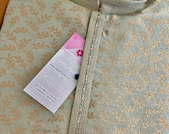 Può includere: Una kurta verde chiaro con un motivo floreale dorato. La kurta ha un colletto alla coreana e una chiusura con bottone. Il tessuto è un broccato con una lucentezza discreta. L'immagine include anche un biglietto da visita con il nome "Kaash Collection" e le informazioni di contatto.