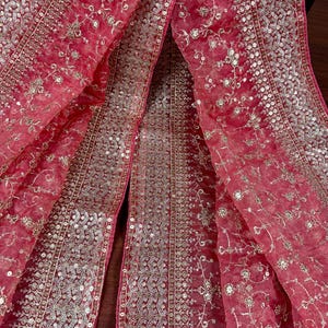 Peut inclure: Un tissu rose vif et transparent, orn&eacute; de broderies florales et de sequins argent&eacute;s. Le tissu est drap&eacute;, mettant en valeur les d&eacute;tails des ornements et la texture d&eacute;licate. Le design pr&eacute;sente un panneau central et des bordures.