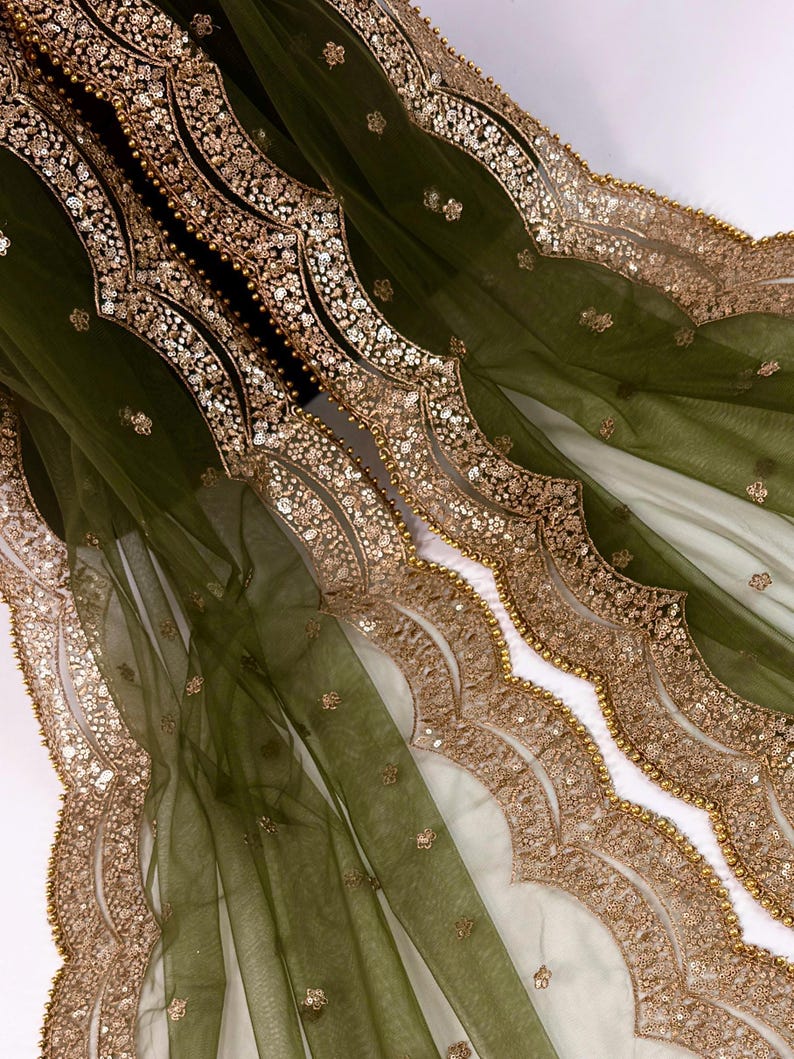 May include: Olive green sheer fabric with ornate gold sequin and bead embellishments. The fabric features a scalloped edge design with intricate detailing. The gold accents create a luxurious and elegant look, suitable for formal wear or decorative purposes.