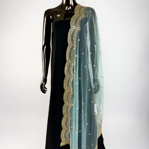May include: A sheer, pale blue dupatta with gold embroidery and embellishments draped over a black dress form. The dupatta has a scalloped edge and scattered gold accents, creating an elegant look.