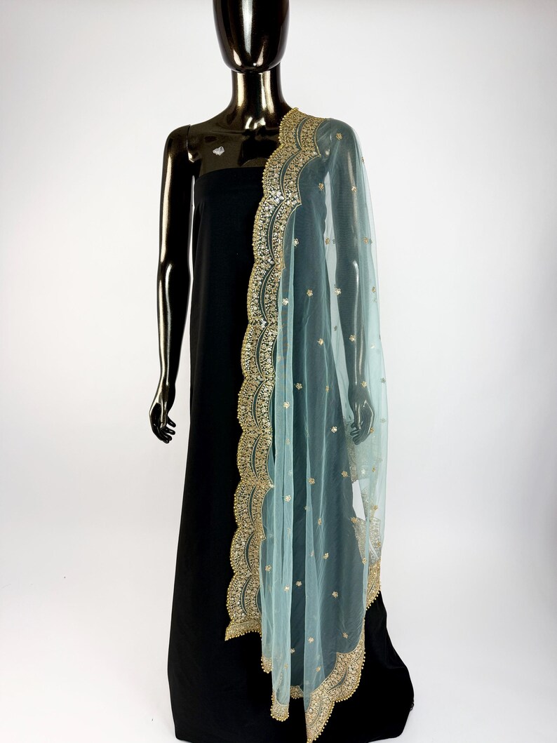May include: A sheer, pale blue dupatta with gold embroidery and embellishments draped over a black dress form. The dupatta has a scalloped edge and scattered gold accents, creating an elegant look.