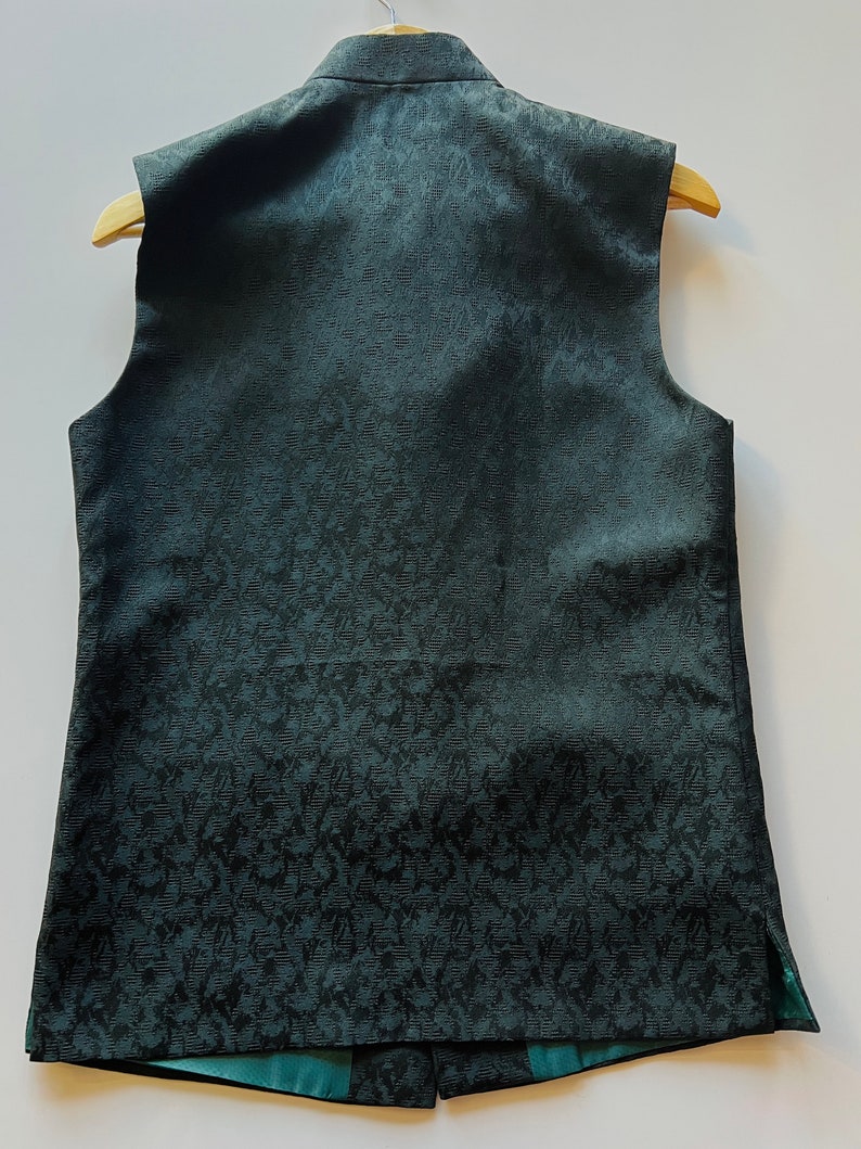 Puede incluir: Un chaleco sin mangas de color verde oscuro con un patr&oacute;n floral. El chaleco tiene un cuello mandar&iacute;n y un cierre de bot&oacute;n.