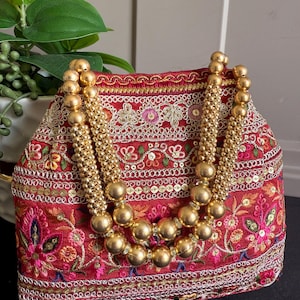 Op de afbeelding: Een rode geborduurde handtas met goudkleurige kralen handvatten en accenten. De tas heeft ingewikkelde bloempatronen in verschillende kleuren en is versierd met pailletten. De goudkleurige kralen handvatten zijn gemaakt van grote, ronde kralen.