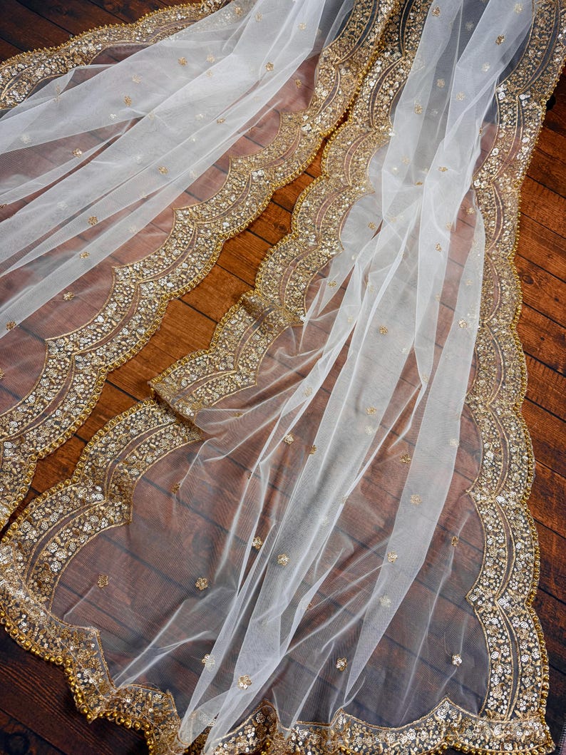 May include: White sheer fabric with a gold beaded trim. The trim features a scalloped design with a repeating pattern of small gold beads and sequins.