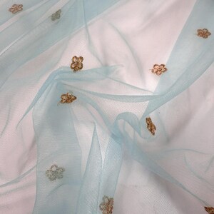 May include: Pale blue tulle fabric with gold floral embroidery. The sheer material is draped, creating soft folds. The delicate embroidery adds a touch of elegance to the fabric, suitable for craft projects or clothing. The fabric is lightweight and airy.