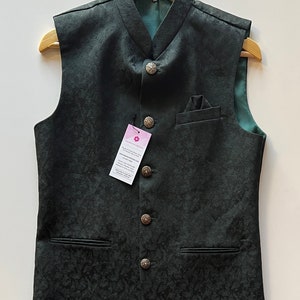 Puede incluir: Un chaleco verde oscuro sin mangas con cuello mandar&iacute;n y cinco botones plateados. El chaleco tiene un sutil estampado floral y dos bolsillos.