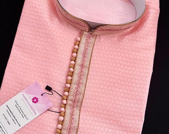 Könnte beinhalten: Eine rosa Kurta mit gold- und rosafarbenem Besatz und Perlenverzierungen. Die Kurta hat einen Mandarinkragen und ein langes, fließendes Design. Das Etikett auf der Kurta lautet "KAASH COLLECTION House of Women, Men & Kids Ethnic Wear www.kaashcollection.com Pleasanton, California 415-827-9482"