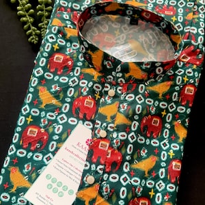 Pode incluir: Conjunto kurta pijama verde com um padrão repetido de elefantes vermelhos e pássaros amarelos. A gola e os punhos têm um design contrastante. A peça de vestuário tem uma frente abotoada e uma etiqueta com o nome da marca e informações de contato.