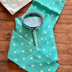 Pode incluir: Uma kurta azul turquesa com um padr&atilde;o geom&eacute;trico branco e prateado. A kurta tem um colar mandarim e um fecho de bot&atilde;o. &Eacute; feita de um tecido macio e leve.