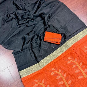 May include: A black saree with a red and gold border. The saree has a subtle shimmer and is decorated with small, black sequins. The border features a repeating pattern of stylized trees.