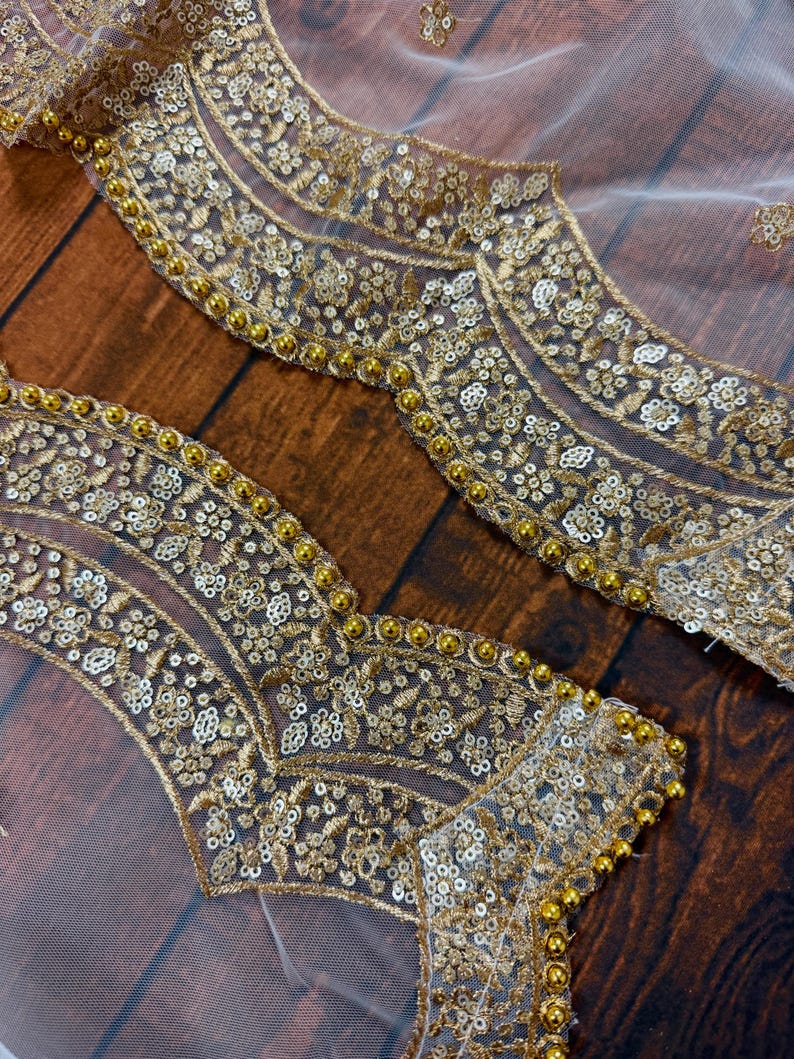 May include: White mesh fabric with gold embroidery and sequins. The fabric has a scalloped edge with gold beads.