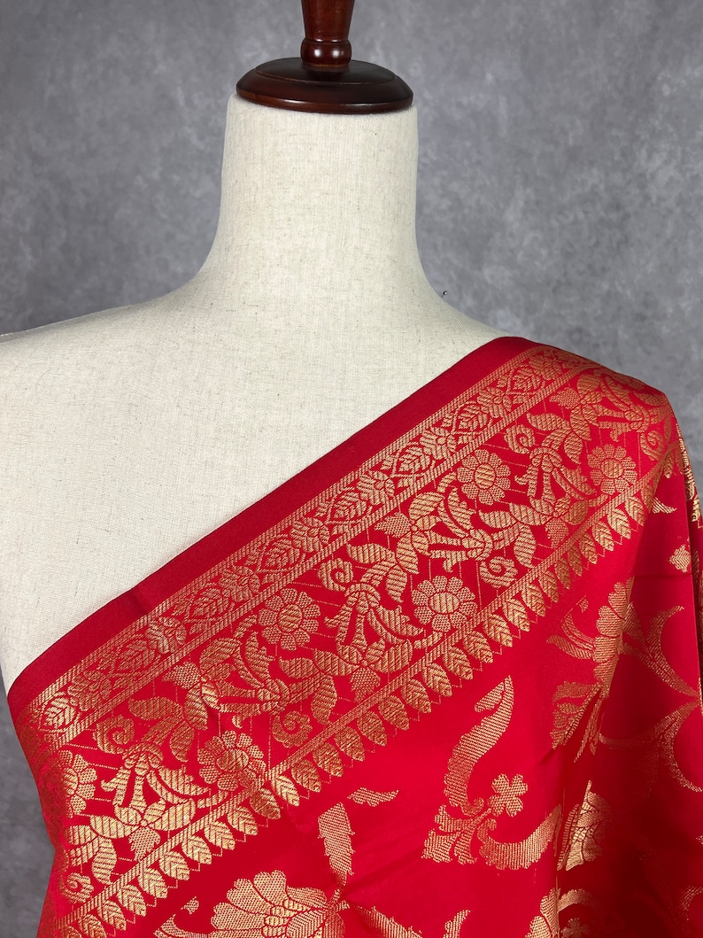 May include: A vibrant red fabric with an ornate gold floral border is draped over a mannequin. The gold pattern features detailed flowers and leaves. The fabric's rich color and intricate design suggest a luxurious textile.