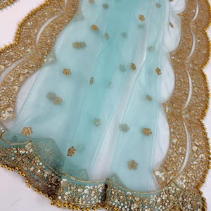 May include: A light blue sheer fabric with a scalloped gold sequin border. The fabric features small gold floral embellishments. The border is detailed with gold sequins and small gold beads.