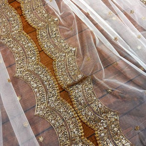 May include: White sheer fabric with a gold sequined border. The border features a repeating pattern of curved lines and small circles.
