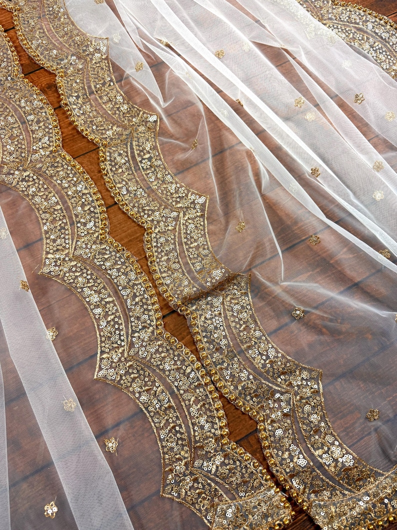 May include: White sheer fabric with a gold sequined border. The border features a repeating pattern of curved lines and small circles.