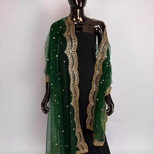 Peut inclure: Un ch&acirc;le vert fonc&eacute; transparent avec une bordure brod&eacute;e dor&eacute;e et des paillettes dor&eacute;es &eacute;parses. Le ch&acirc;le est drap&eacute; sur une robe noire sur un mannequin. La bordure dor&eacute;e a un bord festonn&eacute;.
