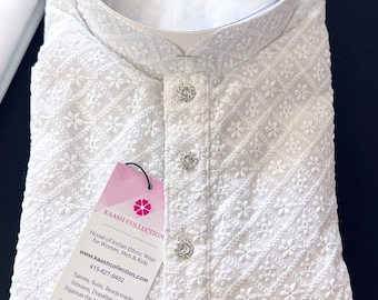 Pode incluir: Kurta branca bordada com gola alta e fecho de botões. A kurta é feita de um tecido leve e apresenta um delicado padrão floral. A etiqueta anexada à kurta diz "Kaash Collection, House of Indian Ethnic Wear for Women, Men & Kids, www.kaashcollection.com, 415-827-9482, Sarees, Suits, Readymade blouses, Dupattas, Kurta Pajamas for Mens and Boys, 405 Boulder Ct, Suite 200-4, Pleasanton, California."